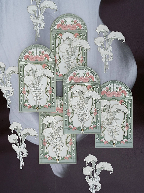 Invitation suite with art nouveau wedding invitations, arched cards featuring calla lily illustration and pink floral borders on gray marble surface