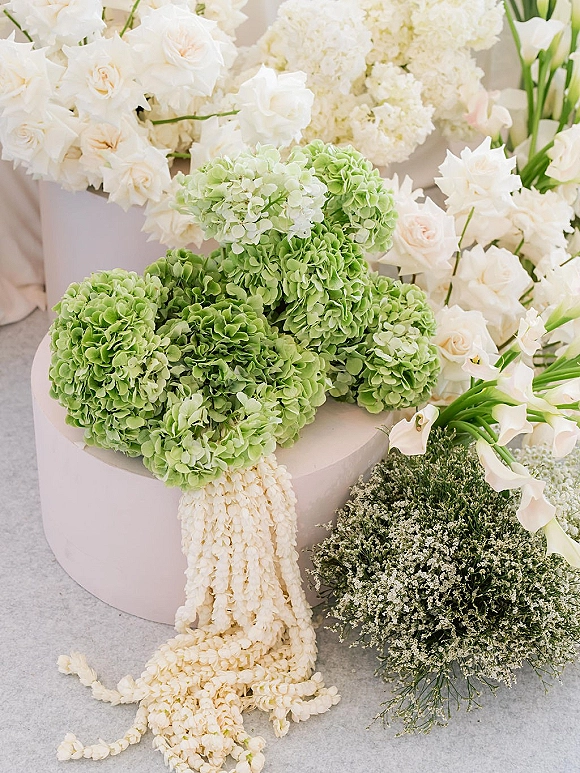 Wedding bouquet with green hydrangea and white roses, calla lilies and baby’s breath resting on a light floor beside a white hat box
