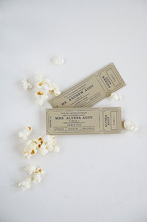 Wedding escort cards in ticket wedding escort cards style with black-and-white typography, scattered popcorn on a white linen tablecloth