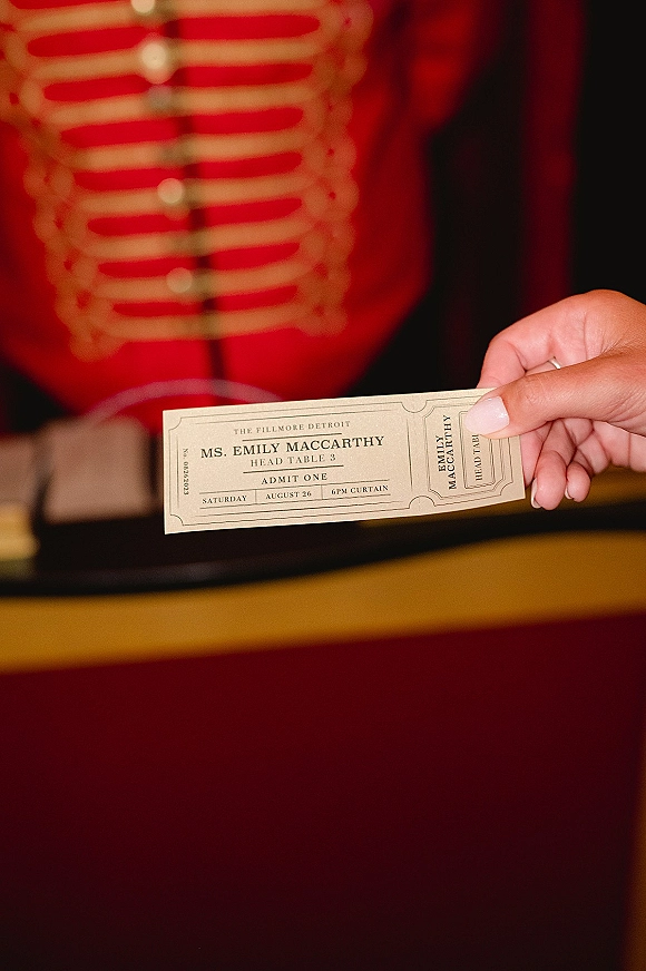 Wedding invitation ticket wedding invitation held in hand with a wedding ring, printed text on a card against a red velvet theater seat background