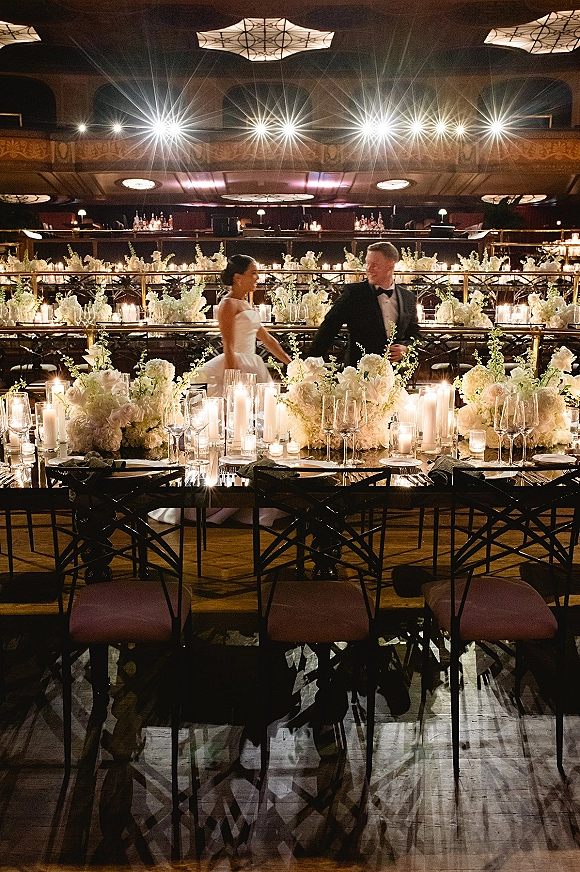 Reception tablescape with candlelit wedding reception glow, white floral centerpieces and pillar candles on long banquet tables in a ballroom mezzanine setting