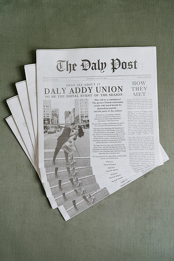 Newspaper wedding program stacked on green fabric, featuring a black-and-white photo, bold headline typography, and printed details