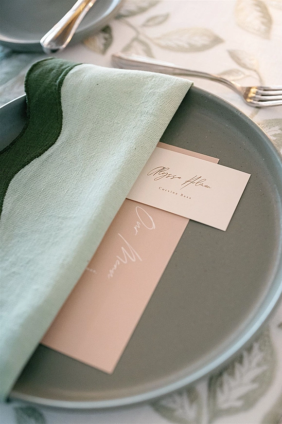 Wedding place setting with a wedding table place setting featuring a gray dinner plate, linen napkin, menu and place card on a patterned tablecloth