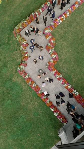 Wedding ceremony aisle with outdoor wedding aisle flowers bordering a zigzag stone path, guests in formal attire on a grass lawn