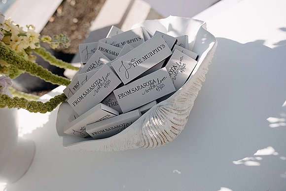 Wedding favors in a shell bowl, personalized matchboxes wedding style, set on a tablecloth with floral arrangement in outdoor light shadows