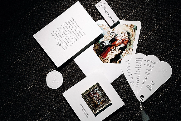 Wedding invitation suite flat lay with black and white wedding invitations, envelopes, wax seal, rings, matchbook, and tassel on dark carpet