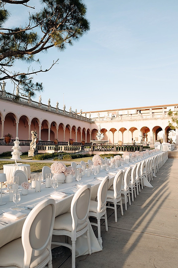 Reception tablescape with long banquet table wedding styling, blush florals and candlelight in an arched courtyard with fountain backdrop