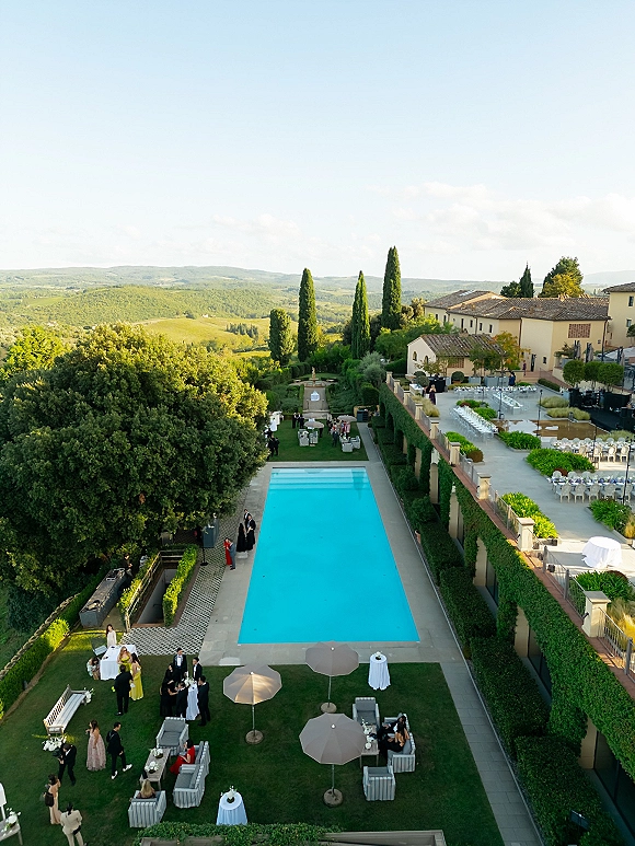 Outdoor reception setup with poolside wedding reception tables in white linens, lounge seating and umbrellas on a villa terrace with string lights
