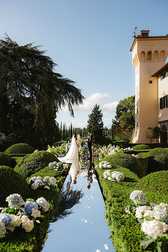 Wedding ceremony with bride and groom exchanging vows on a mirrored aisle runner, hydrangea florals and villa garden backdrop