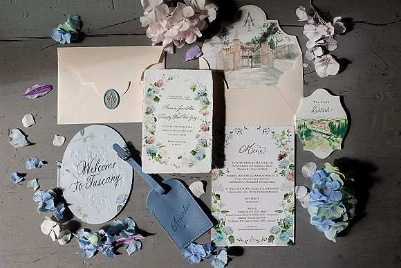 Invitation suite with a deckled edge wedding invitation, wax seal, watercolor cards and envelopes, styled on a gray wooden tabletop with hydrangea petals