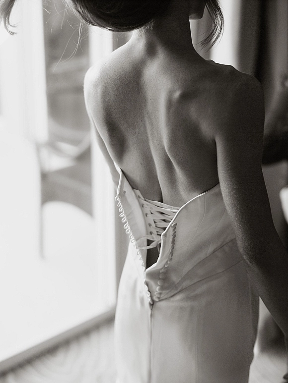 Wedding dress back with corset back wedding dress lacing and fabric-covered buttons, lit by window light in an interior room
