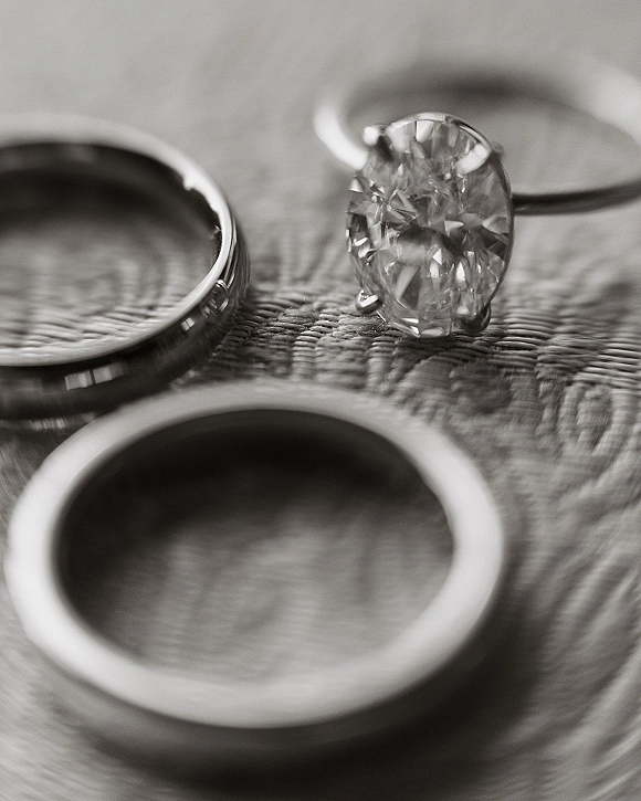 Wedding rings and engagement ring close up in a three-ring stack with a diamond solitaire, resting on textured fabric backdrop