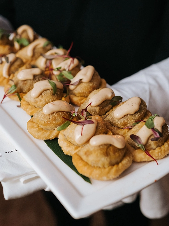 Wedding appetizers on a passed hors d'oeuvres tray, bite-sized savory pastries with creamy sauce drizzle and microgreens garnish at reception