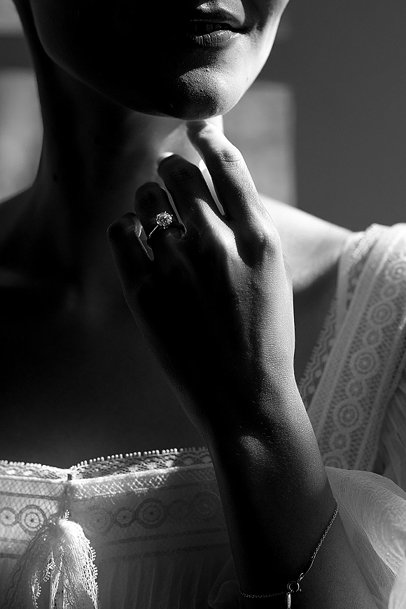 Engagement ring close-up of a hand wearing a diamond solitaire ring, lace wedding dress sleeve and bracelet lit by window light