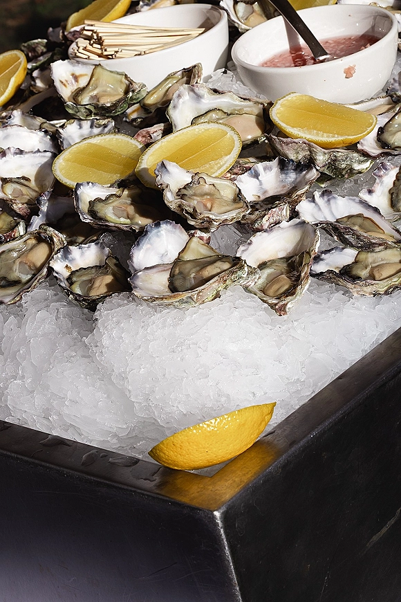 Oyster bar display with oysters on the half shell on crushed ice and lemon wedges, served on a tray atop a buffet table