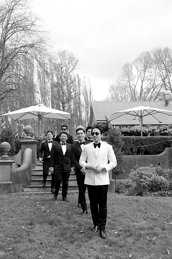Groomsmen portrait of the groom with groomsmen in tuxedos and bow ties, one in a white dinner jacket, on stone steps in a garden lawn setting