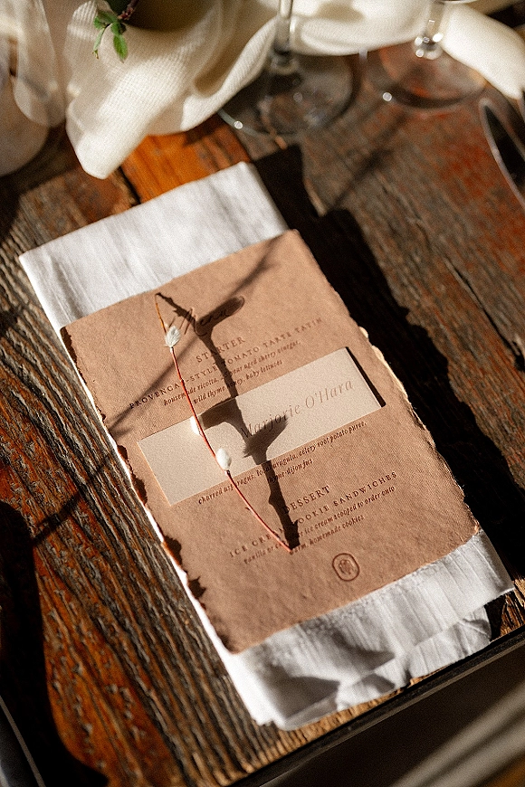 Wedding menu card with rustic wedding menu styling on deckled edge paper, paired with a name card on a napkin on a wooden table