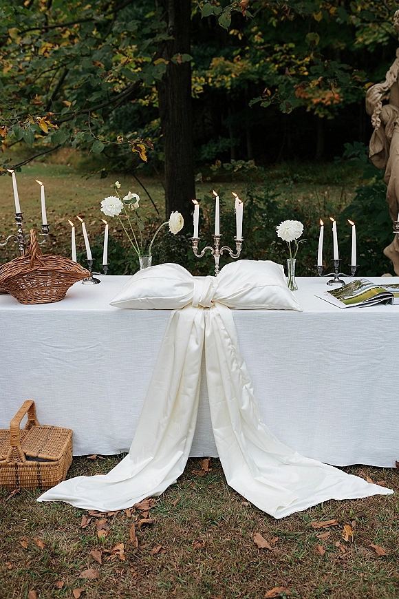 Wedding sweetheart table styled with outdoor sweetheart table decor, white cloth and satin bow, candles and candelabras on a garden lawn
