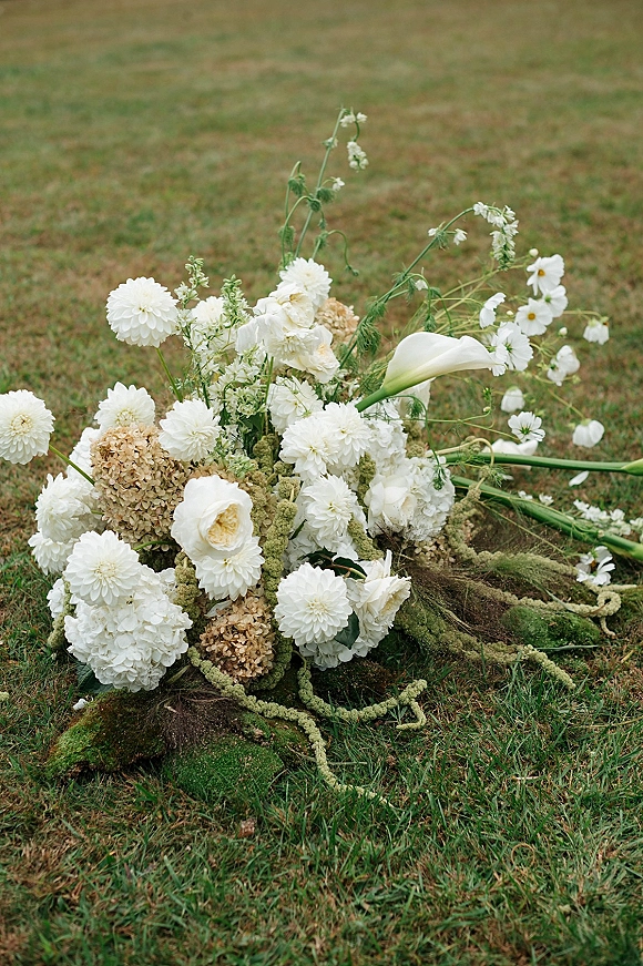 Bridal bouquet with white wedding bouquet blooms like calla lily, dahlias and hydrangea, nestled in moss on a grass lawn