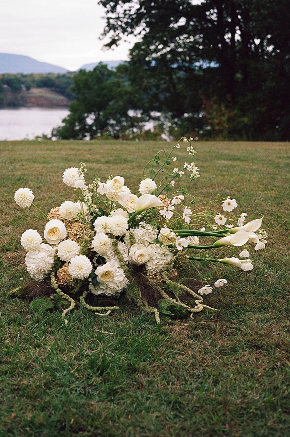 Wedding ceremony flowers in a ground floral arrangement of white calla lilies, dahlias, roses, hydrangeas and moss on a lakeside lawn