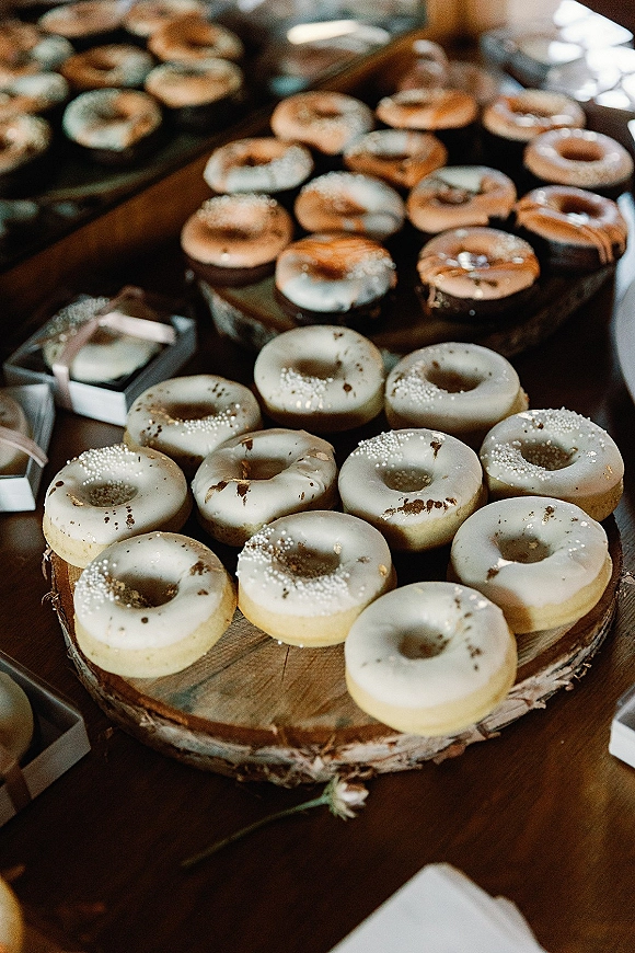 Wedding donuts arranged on a wooden cake stand with glazed donuts and donut holes on a rustic dessert display table