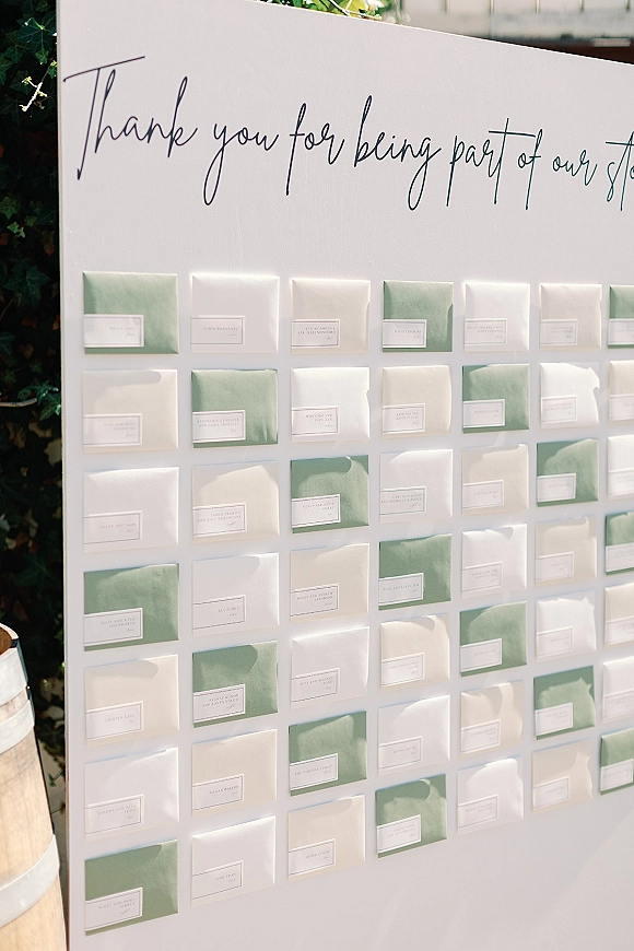 Wedding seating chart envelope seating chart display with calligraphy sign and mounted envelope place cards on a sunlit patio greenery hedge background