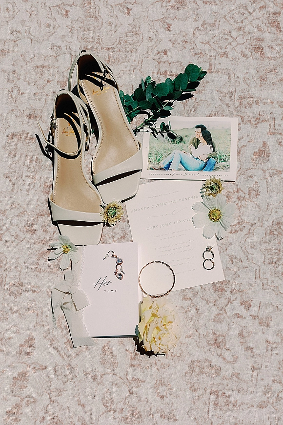 Invitation suite wedding invitation flat lay with save the date, vow booklet, rings, shoes and earrings on a patterned rug with ribbon accent