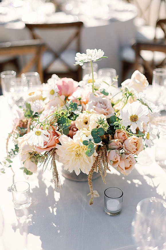 Wedding centerpiece with pastel wedding centerpiece florals—blush roses, white cosmos, dahlia, eucalyptus—in a low compote vase on a white tablecloth