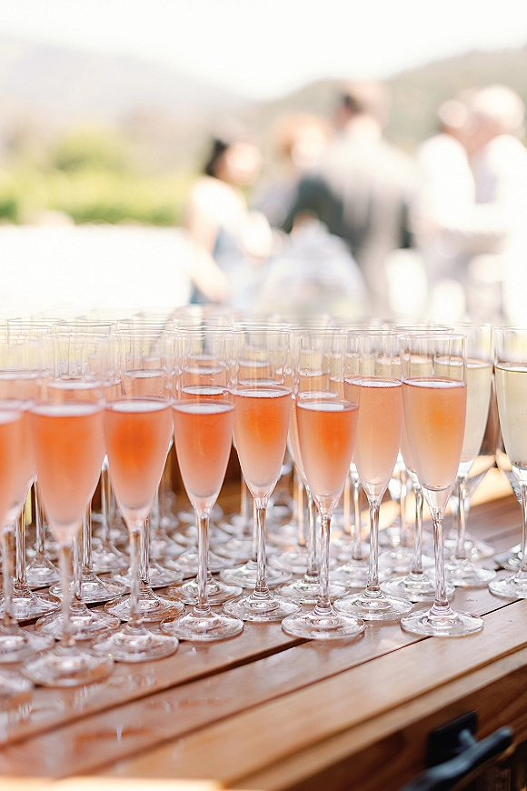 Welcome drinks set out on a wooden table with champagne flutes of sparkling wine and rosé, with mountain views and guests outdoors