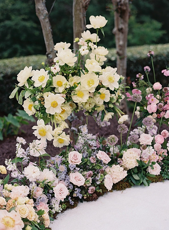 Ceremony floral arrangements with wedding aisle florals of white blooms and blush roses in a meadow-style installation among tree trunks and garden foliage