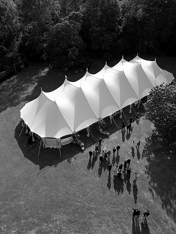 Wedding tent setup with a white sailcloth outdoor wedding tent, tie-back drapes, lattice panel, and floral entry on a wooded lawn