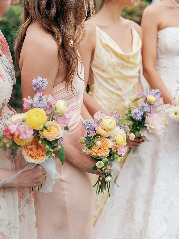 Bridesmaid bouquets of pastel bridesmaid bouquets with ranunculus, garden roses, sweet peas and greenery, held outdoors in soft light