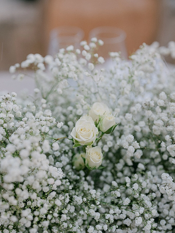 Baby's breath centerpiece with gypsophila wedding centerpiece blooms and white roses in glass vases on a table against a wood wall