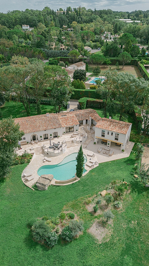 Wedding venue aerial view of a villa wedding venue with a swimming pool, stone patio seating, terracotta roofs, and cypress-lined lawns on a hillside