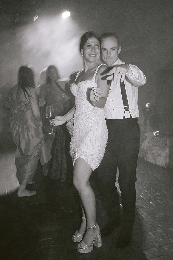 Wedding reception dancing as bride and groom move on a smoky dance floor, her beaded mini dress and platform heels under stage lights
