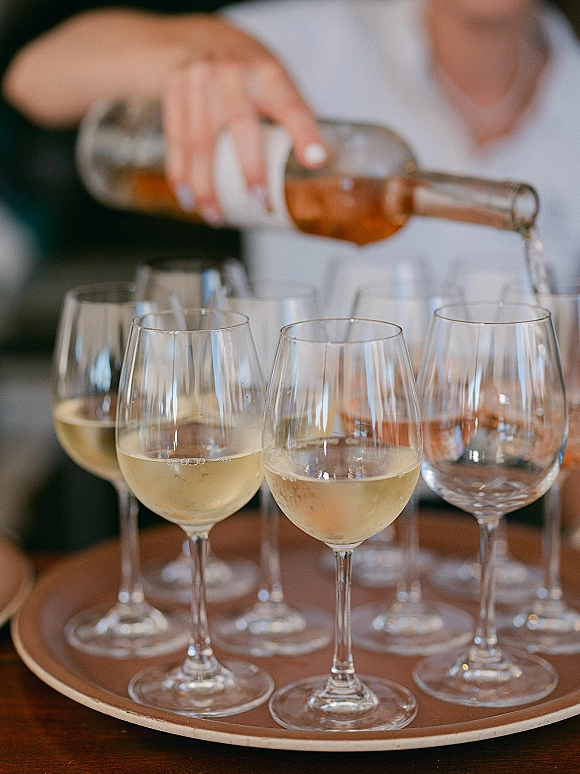 Wedding drink service as a person pours rosé wine into glasses on a serving tray beside a wine bottle on a tabletop
