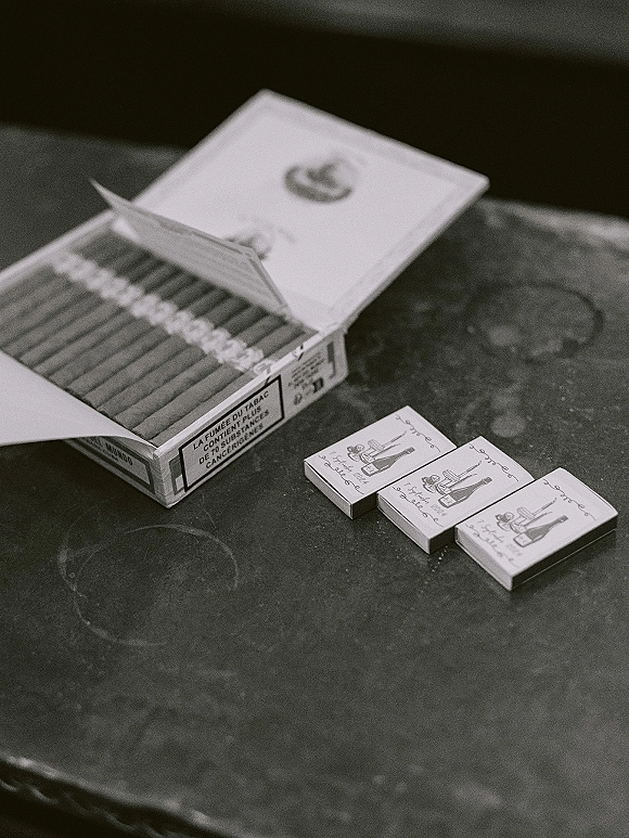 Wedding matchboxes with illustrated labels beside a cigarette pack on a stone tabletop, personalized wedding matchbooks styled as favors
