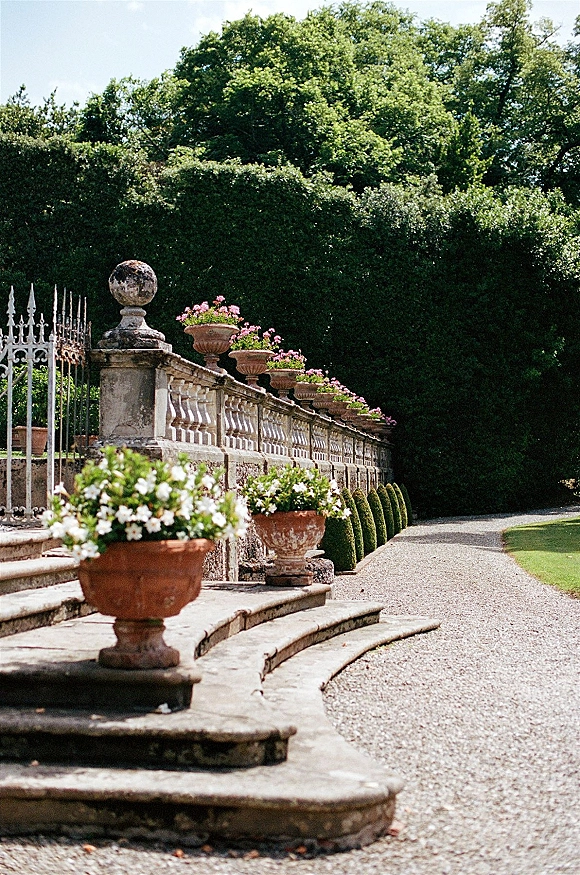 Garden walkway decor at a wedding venue entrance with terracotta planters of pink and white flowers flanking stone steps and gate