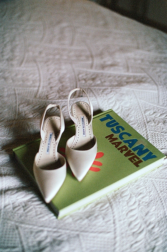 Bridal shoes in a wedding shoes flat lay, white slingback heels beside a book on a textured bedspread in soft natural light