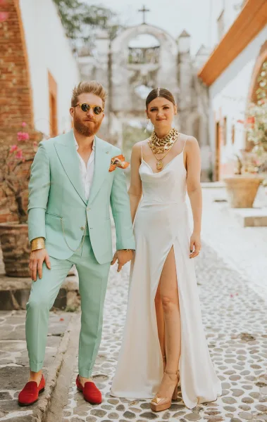 Couple portrait of bride and groom street portrait, bride in satin slip dress beside groom in mint suit on cobblestone street by church facade