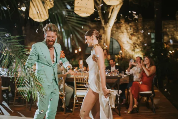 First dance at an outdoor wedding reception as bride in a satin slip dress twirls with groom in mint suit under lantern lights and confetti