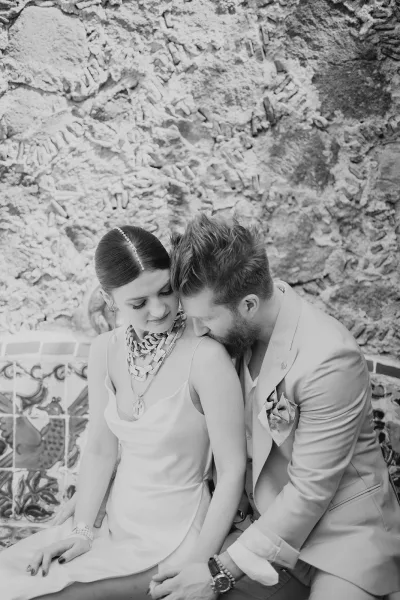 Couple portrait in a black and white wedding portrait, bride and groom embrace with foreheads touching on a patterned tile bench by a stucco wall