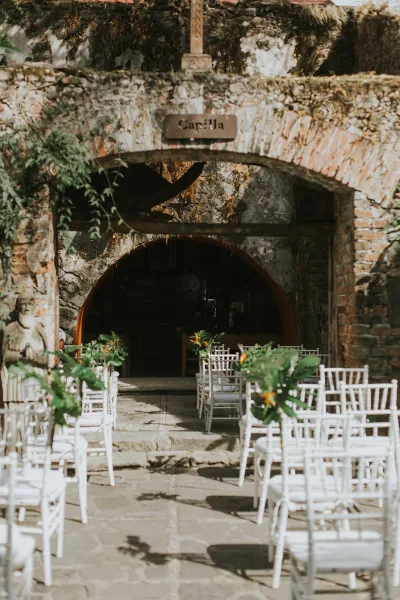 Ceremony aisle decor with an outdoor ceremony aisle of white chairs, greenery and orange flowers leading to a stone arch chapel entrance