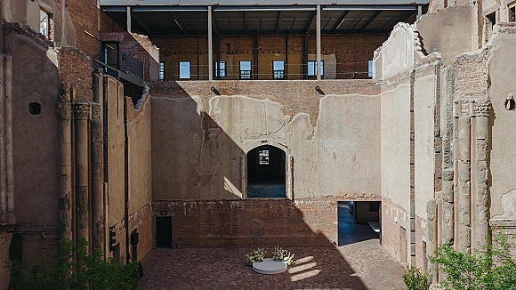 Wedding ceremony setup with an accent of a circular platform and floral arrangements in a brick courtyard ruins, lit by sunlit shadows