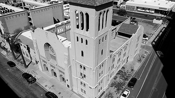 Wedding venue exterior of a church wedding venue with arched windows and a bell tower on a city street lined with palm trees