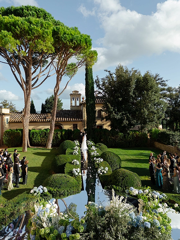 Ceremony aisle design with a mirrored wedding aisle runner, hydrangea and white florals, petal-strewn path on manicured lawn by a villa
