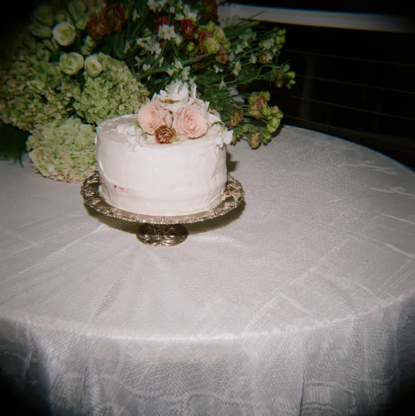 Wedding cake, small wedding cake with textured white frosting and blush rose floral topper on a silver stand beside a large arrangement