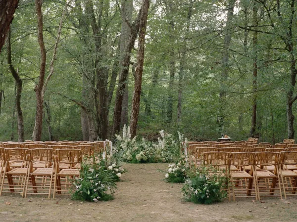 Ceremony aisle decor with white ground florals and greenery garlands leading to an altar floral meadow in a wooded clearing