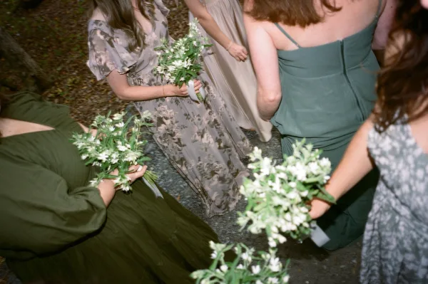 Bridesmaid bouquets of white and green blooms with ribbon wraps held by mismatched dresses as bridesmaids walk along an outdoor path