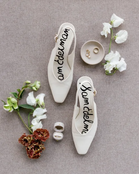 Bridal shoes, white slingback heels styled with wedding rings and pearl drop earrings beside a ceramic dish on a linen backdrop